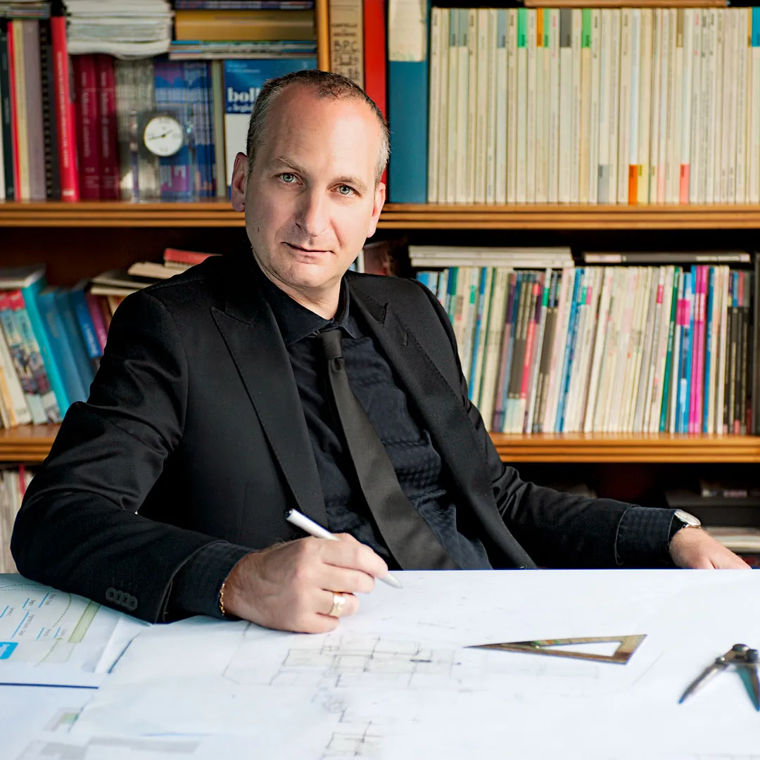 L’architetto Massimo Rodighiero al tavolo da disegno, davanti alla libreria dello studio