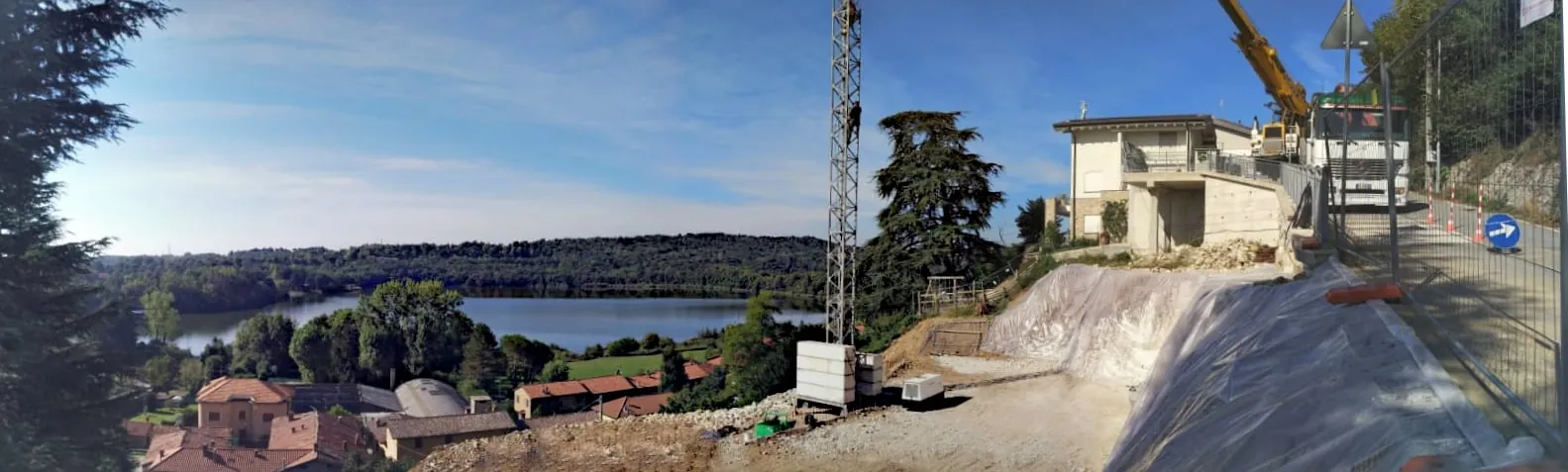 Cantiere di una villa su un terreno in pendio, con la gru, il terrapieno e la vista sul lago e sulle colline boscose