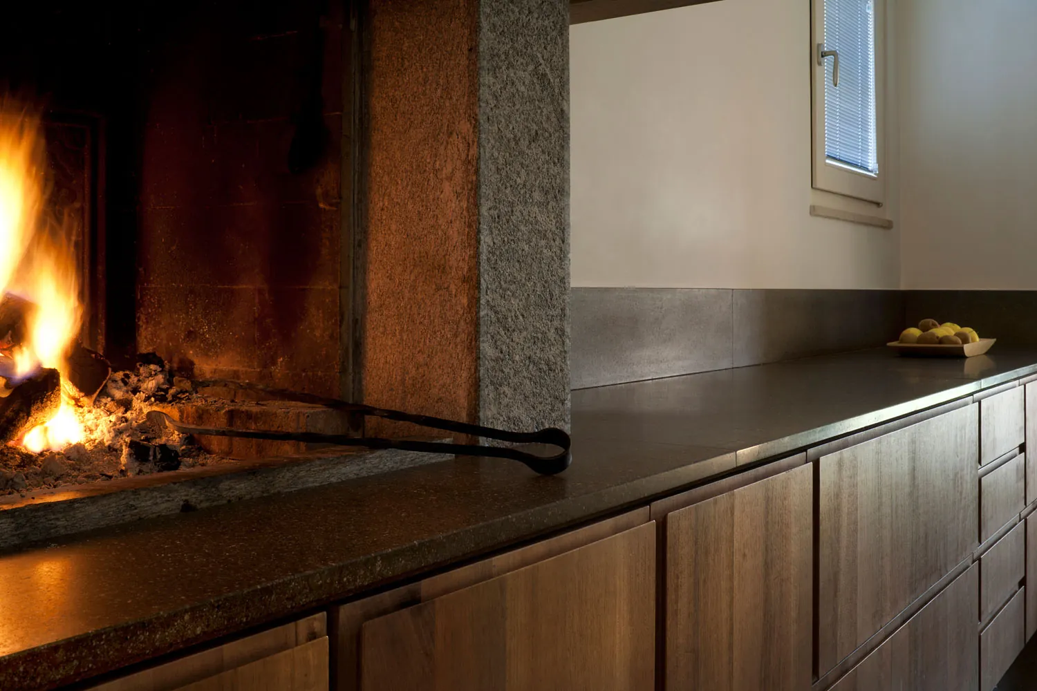 Il camino acceso accanto al piano cucina in pietra scura e legno