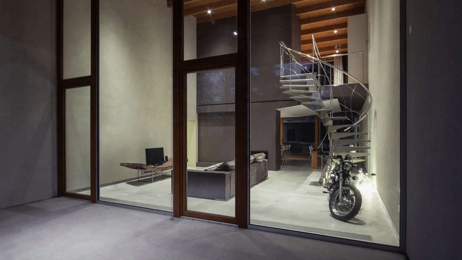 Il soggiorno con la scala e una motocicletta dietro la vetrata