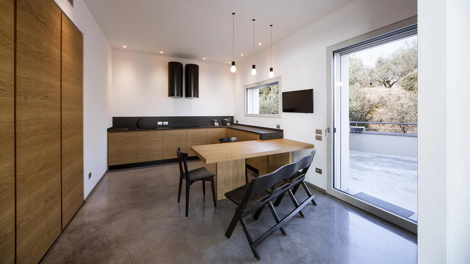 Cucina con armadiatura in legno e tavolo, aperta sulla terrazza