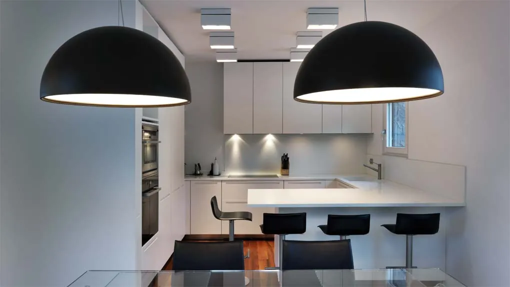 Cucina bianca con penisola e grandi lampade nere a sospensione