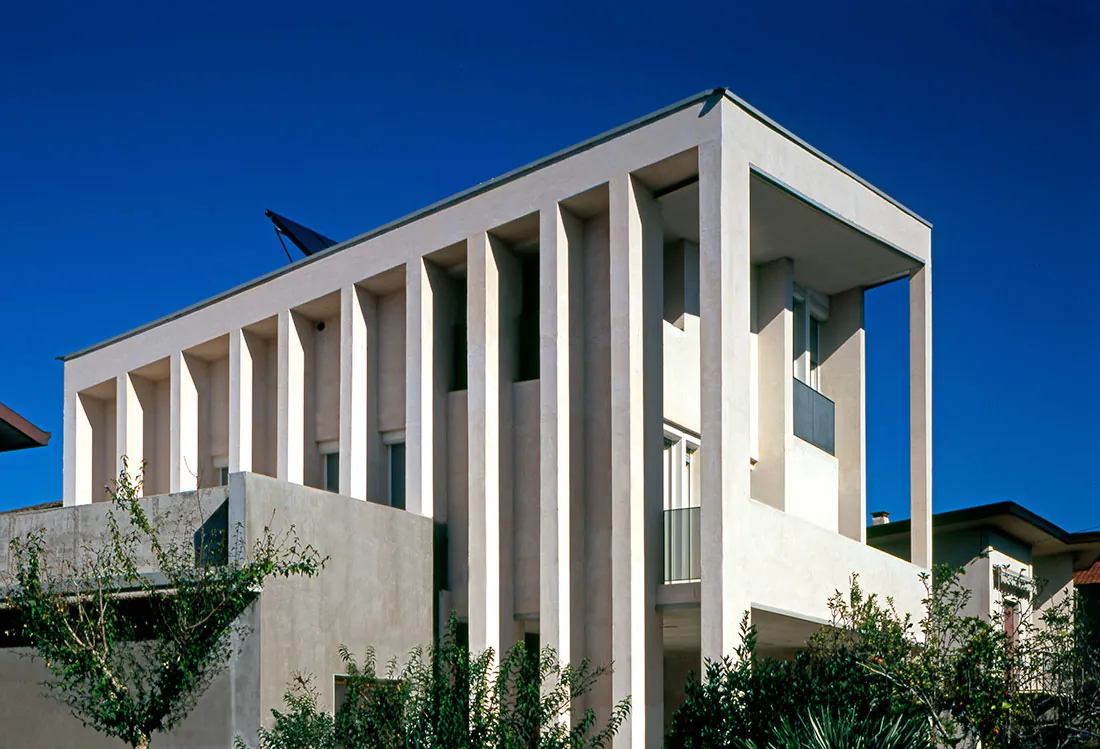 Villa ecosostenibile: la facciata a pilastri bianchi e il giardino, sotto il cielo blu