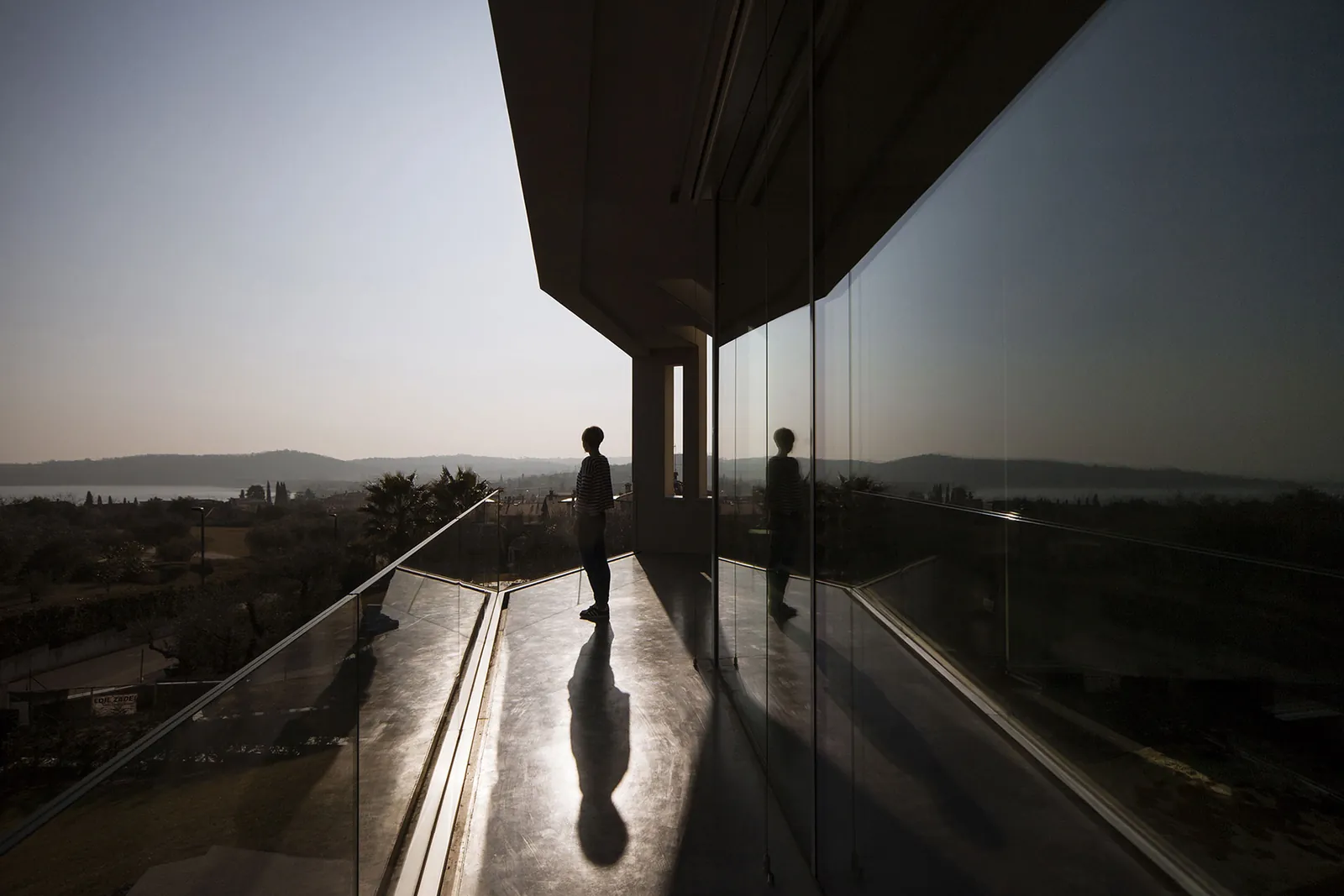 Interno di una villa con la parete vetrata sul lago e una persona controluce sulla terrazza