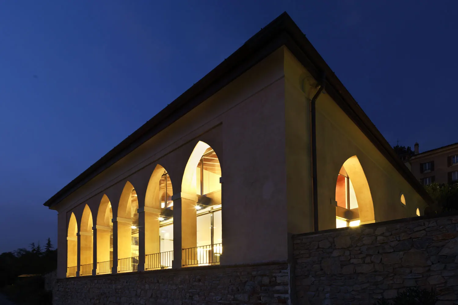 Ristrutturazione di un edificio storico a Brescia: il portico ottocentesco di notte, con le arcate vetrate illuminate
