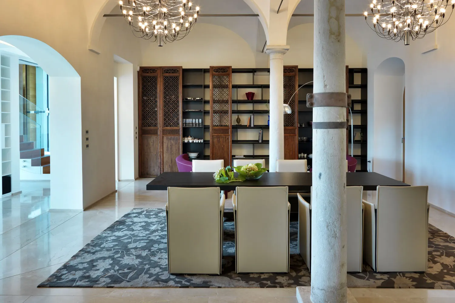 Sala da pranzo con colonna in pietra, volte bianche, lampadari e libreria in legno