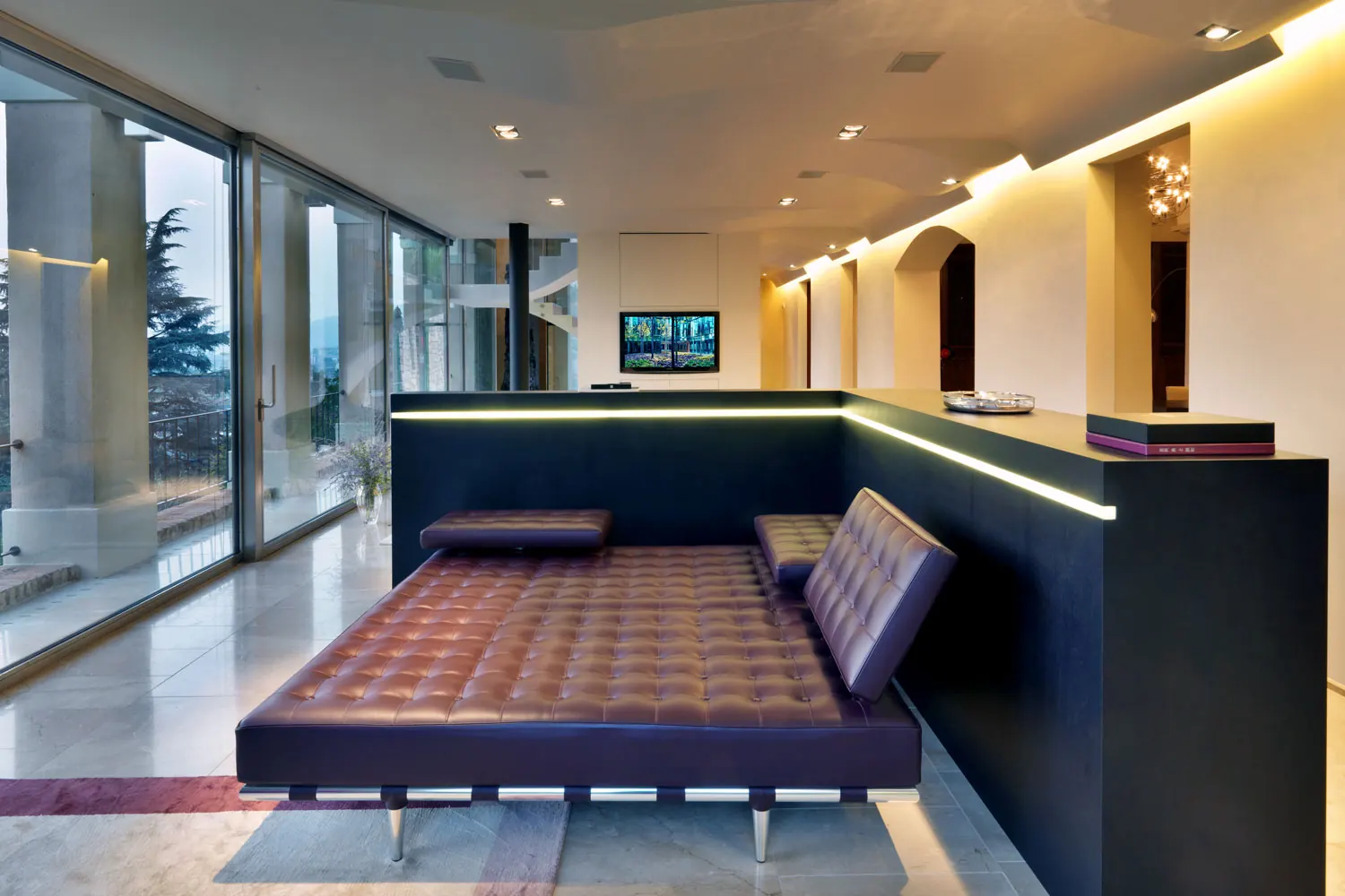 Soggiorno con chaise longue in pelle, mobile basso illuminato e vetrate sul panorama